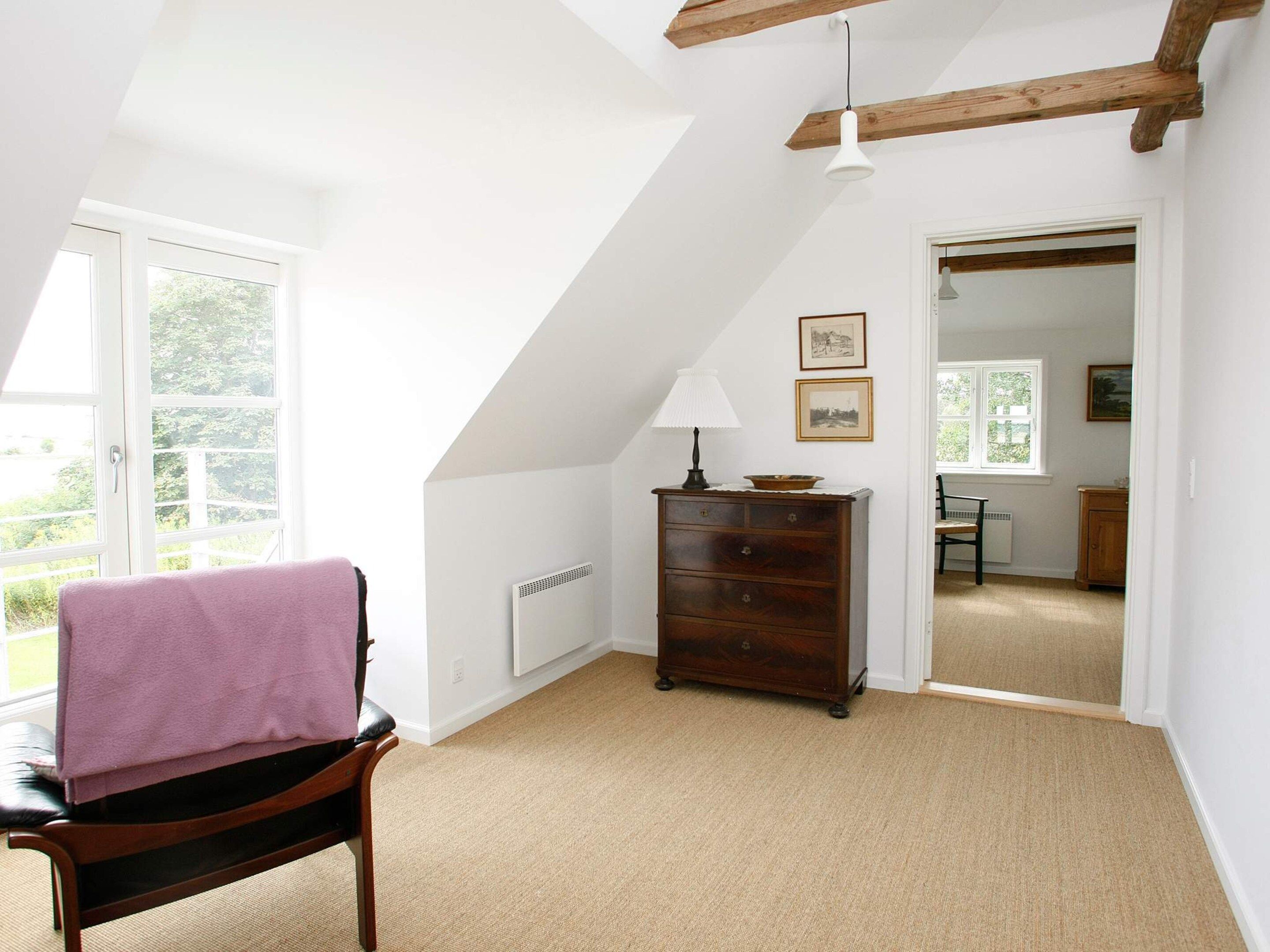 A room with a sloped ceiling, a wooden chair with a pink towel, a dresser, and a lamp.