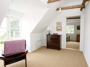 A room with a sloped ceiling, a wooden chair with a pink towel, a dresser, and a lamp.