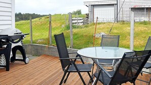 Um deck ao ar livre com mesa de vidro redonda e quatro cadeiras, churrasqueira e deck de madeira.