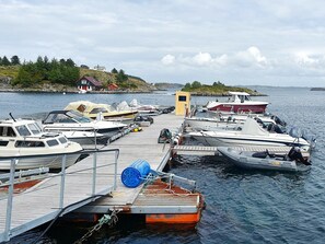 Un muelle con varias embarcaciones amarradas, una pequeña estructura amarilla y un edificio rojo en una colina al fondo.