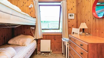 A cozy cabin room with a bunk bed, a desk with a lamp, and a window with curtains.