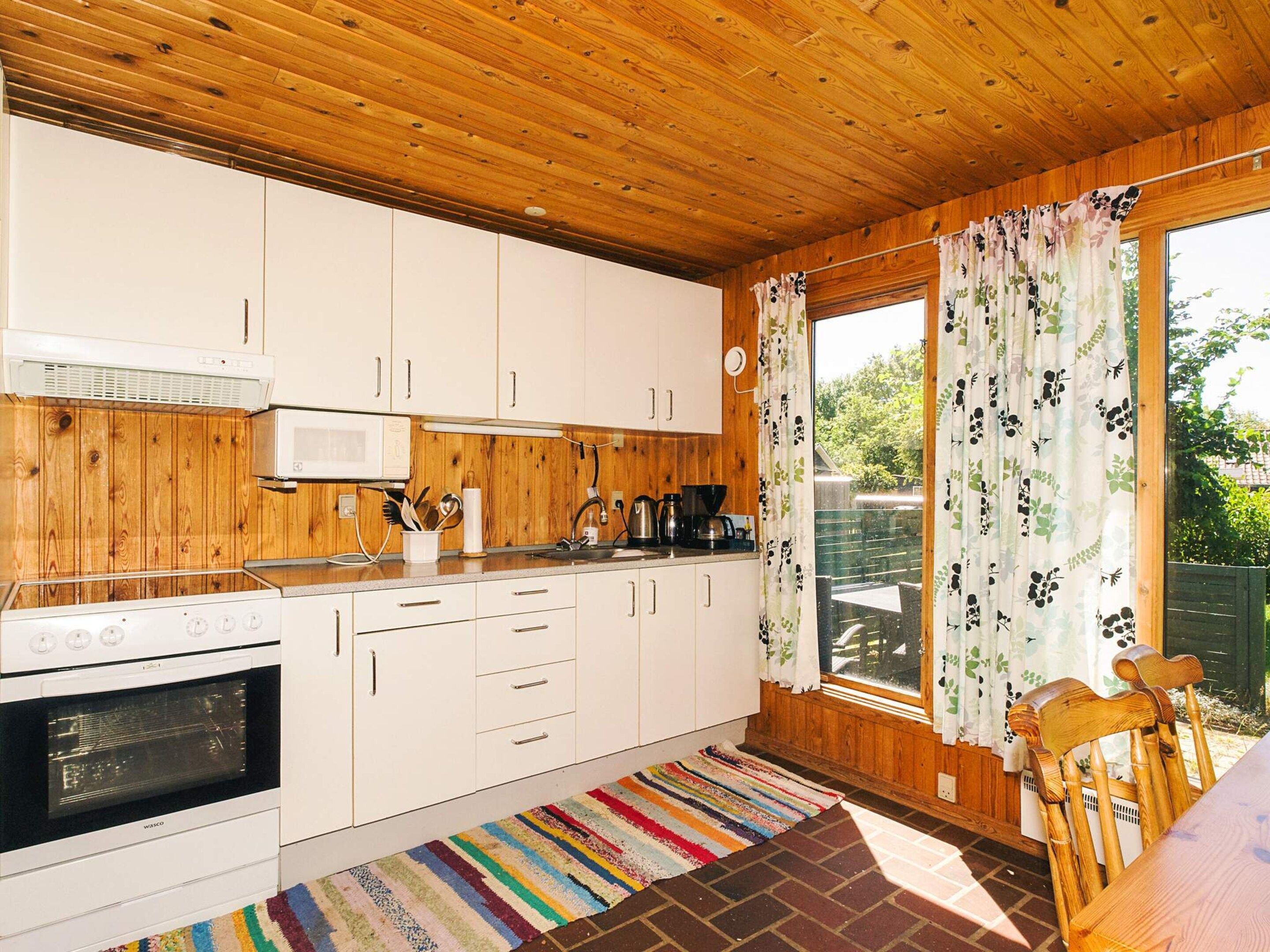 A compact kitchen with wooden paneling, white cabinets, a microwave, a stove, and a window with floral curtains.