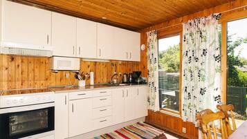 A compact kitchen with wooden paneling, white cabinets, a microwave, a stove, and a window with floral curtains.