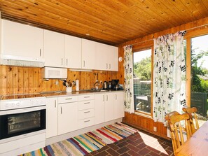 Cocina compacta con paneles de madera, armarios blancos, microondas, estufa y ventana con cortinas florales.