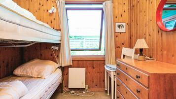 A bunk bed room with a window, a desk with a lamp, and a dresser.