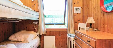 A bunk bed room with a window, a desk with a lamp, and a dresser.