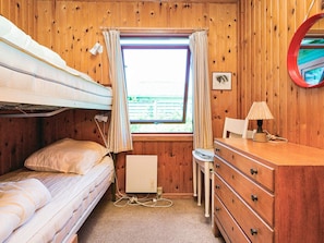 A bunk bed room with a window, a desk with a lamp, and a dresser.