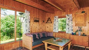 L’intérieur chaleureux d’un chalet, avec un décor en bois, un canapé, une table et une fenêtre donnant sur un paysage verdoyant.