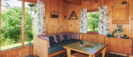 Interior acolhedor de uma cabana com decoração em madeira, um sofá, uma mesa e uma janela com vista para o verde.