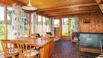 A wooden cabin with a dining area, a television, and large windows.