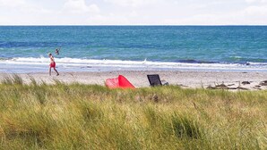 Une plage avec une tente rouge et une chaise noire sur le sable, et une personne qui marche en direction de l’eau.