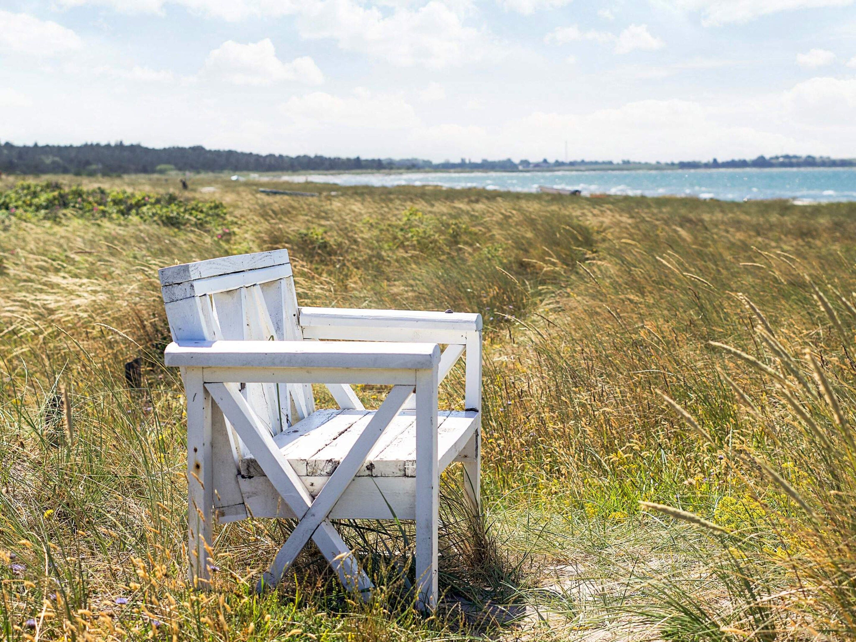 Een witte strandstoel in een grasveld met uitzicht op de zee en een verre kustlijn.