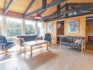 A spacious room with wooden beams, a large window, a sofa, a chair, and a table.