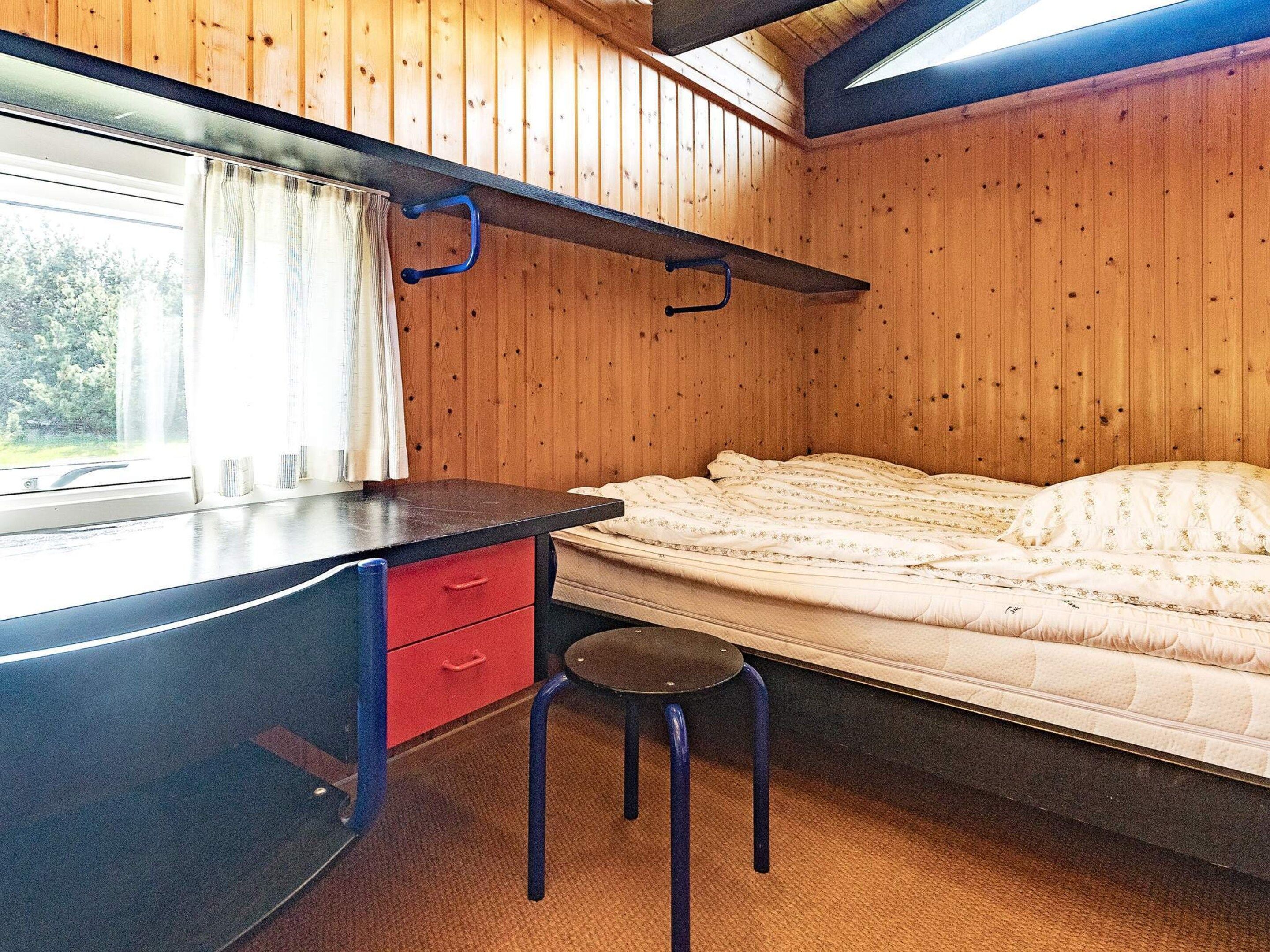 Un dormitorio pequeño con cama, escritorio y silla, además de un ventanal.