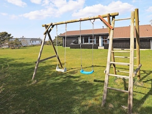 A wooden swing set in a grassy yard with a building in the background.