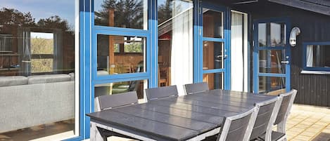 An outdoor dining area with a table and chairs, large windows, and a door.