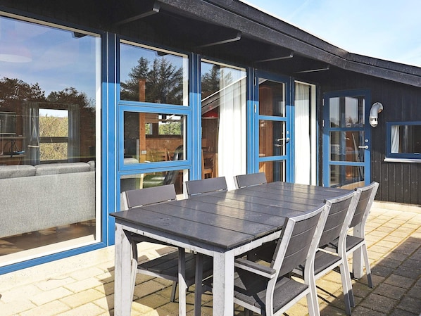 An outdoor dining area with a table and chairs, large windows, and a door.