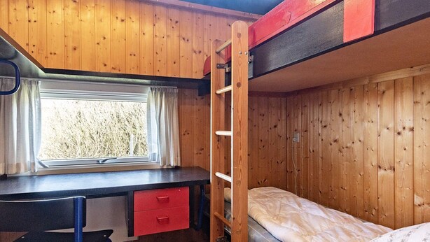 A bunk bed with a desk and chair, a window with curtains, and a ladder.