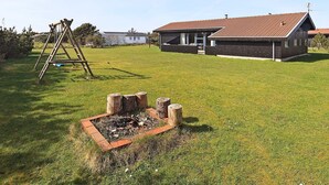 A residential property with a fenced yard, a wooden swing set, and a house with a red-tiled roof.