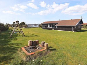 A residential property with a fenced yard, a wooden swing set, and a house with a red-tiled roof.