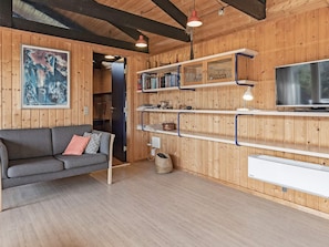 A cozy living room with a grey sofa, wooden walls, and a mounted TV.
