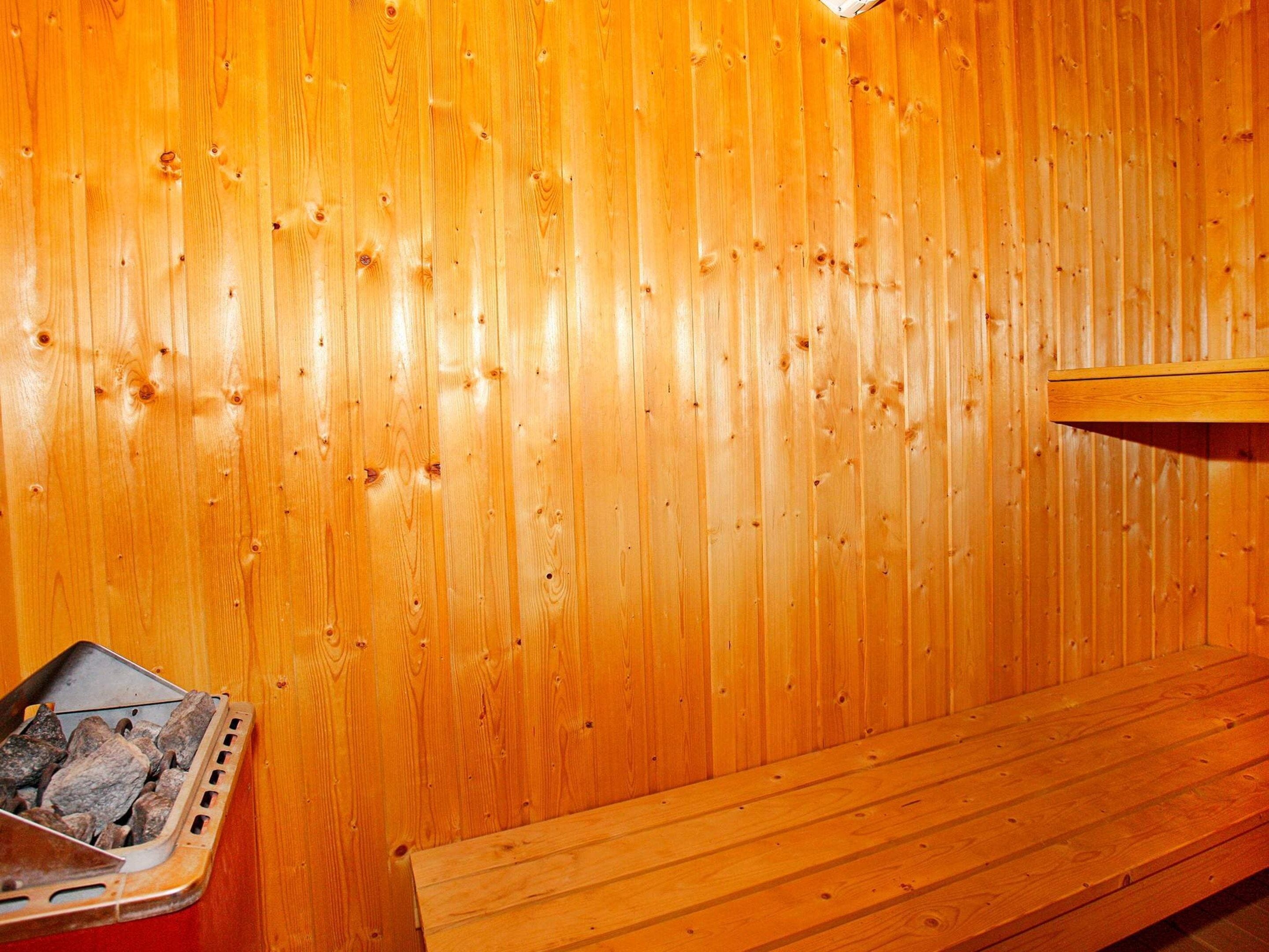 A wooden sauna with a bench and a metal container, likely for holding stones or rocks.