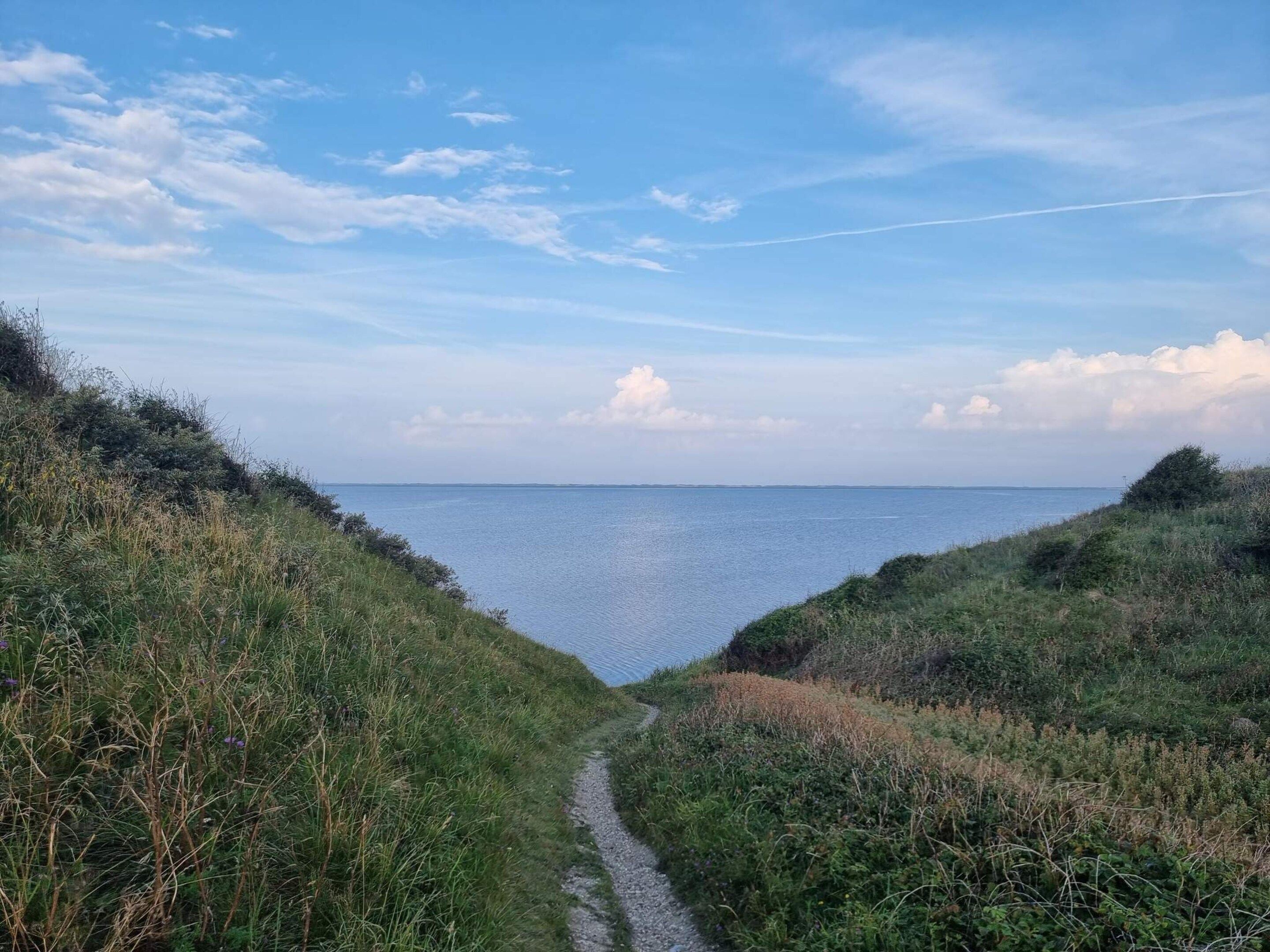Camino costero que lleva a una masa de agua bajo un cielo despejado.
