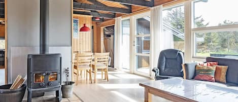 A cozy room with a wood-burning stove, wooden furniture, and large windows.
