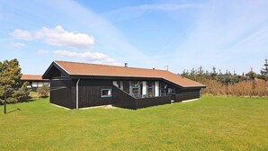 A two-story house with a sloped roof, a front porch, and a fenced yard. - 8 Person Holiday Home in Vestervig (Vestervig)