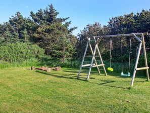 A wooden swing set in a grassy area with trees in the background.