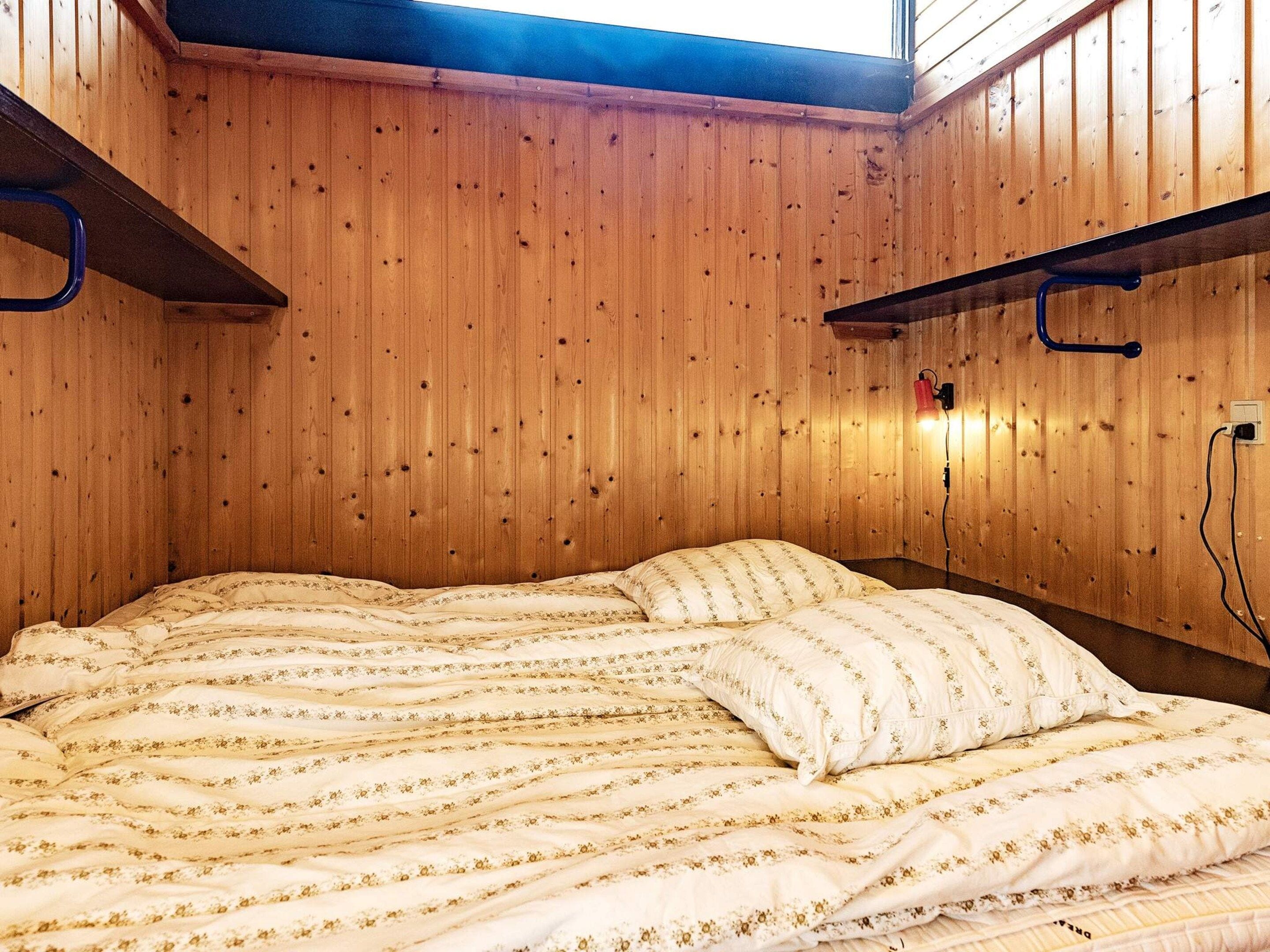 Una habitación con paredes de madera, una cama con ropa de cama floral y un tragaluz.