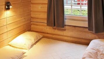 A cozy cabin room with a wooden interior, a bed with white bedding, a pillow, and a nightstand with a lamp.