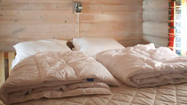 A wooden cabin room with a bed, a wall-mounted light, and a window with curtains. - 8 Person Holiday Home in Trysil (Trysil)