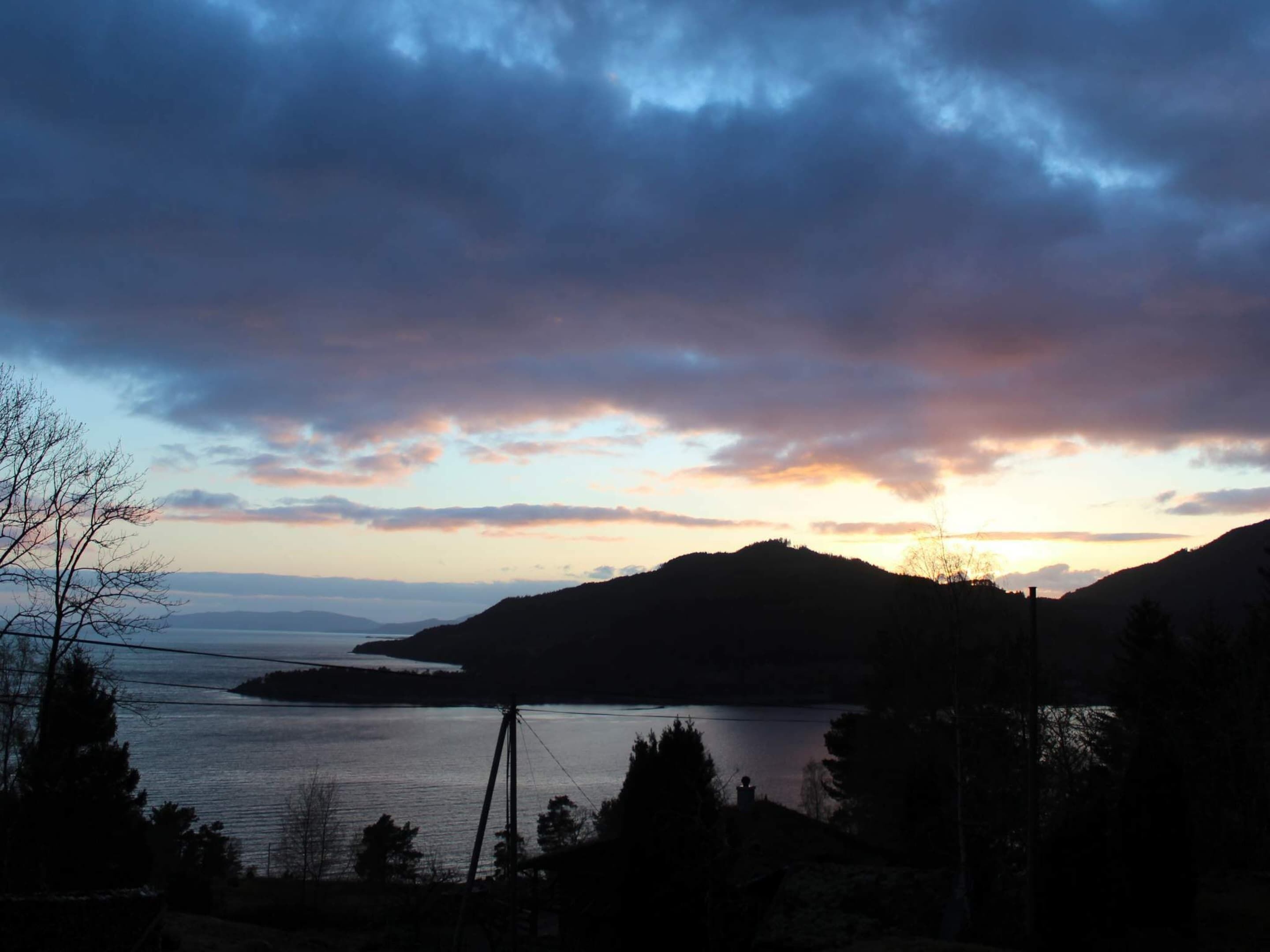 A lakeside view with hills in the background and a cloudy sky.