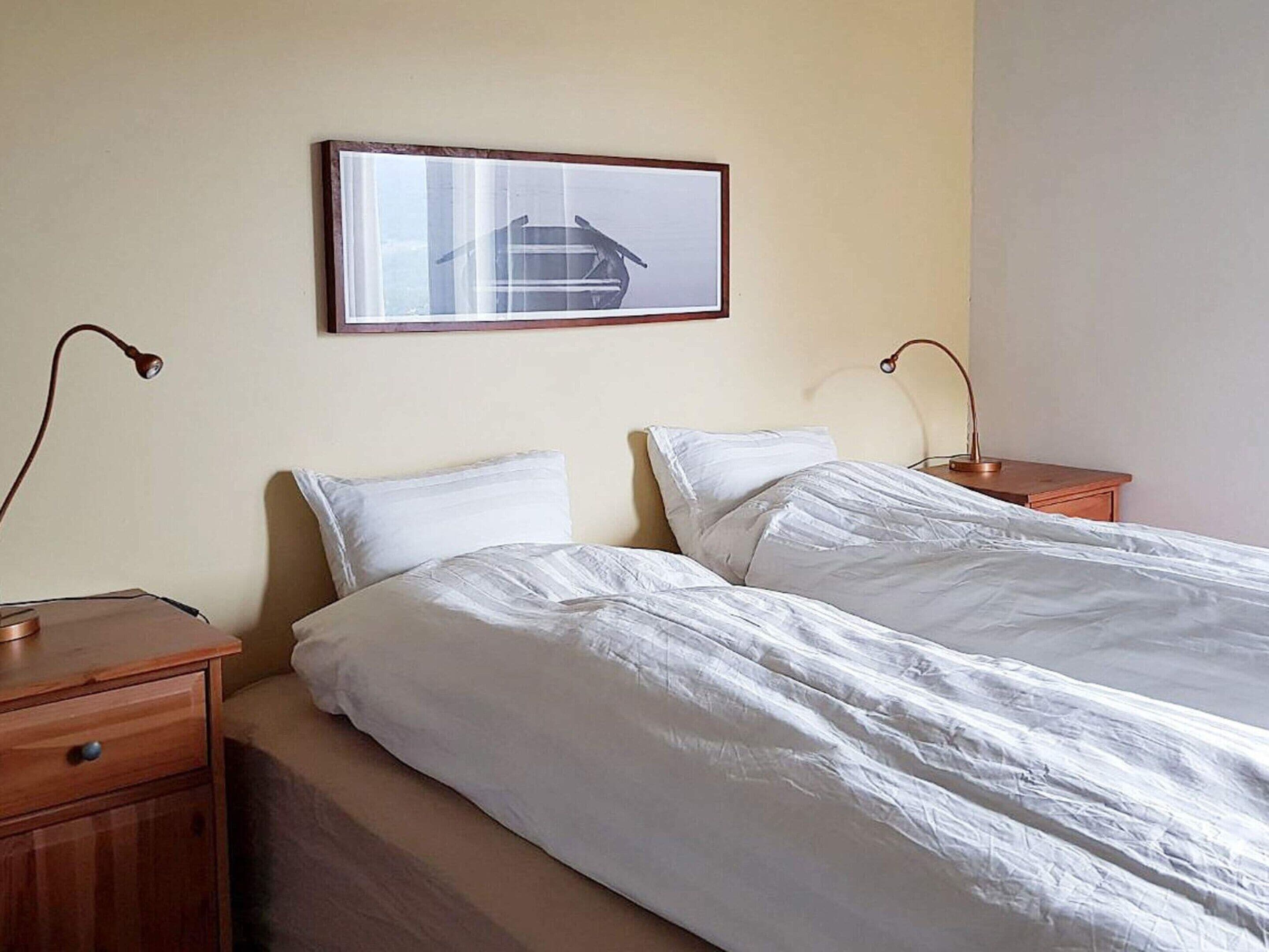 A hotel room with two single beds, wooden nightstands, and a framed picture on the wall.