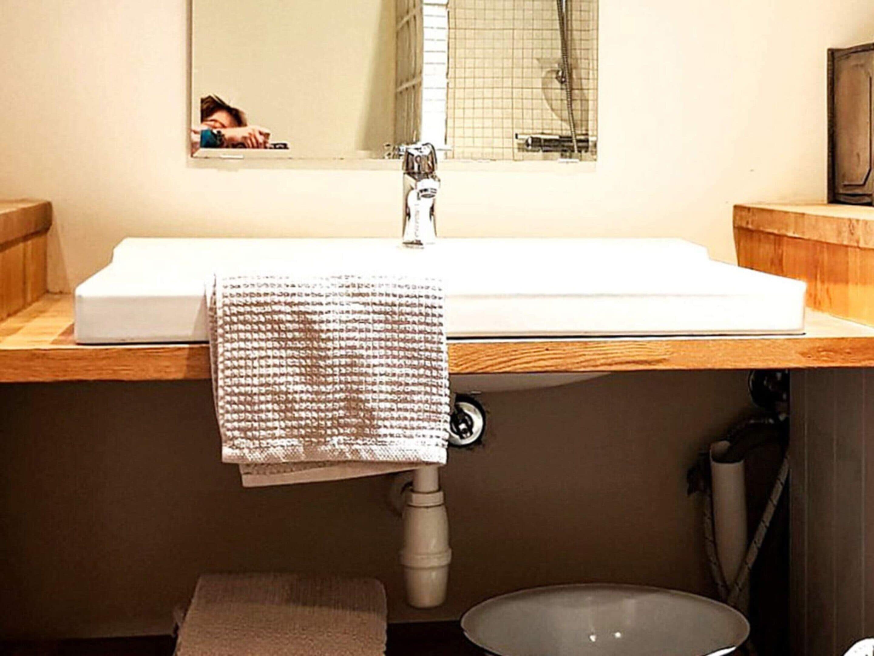 Une salle de bain avec un lavabo blanc, un plan de toilette en bois et un miroir au-dessus.