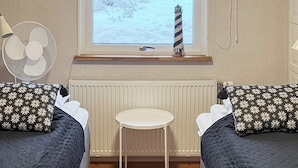 A room with two beds, a small round table, a window with a view of a lighthouse, and a radiator. - Holiday Home in Lidköping (Lidköping)