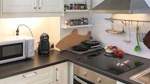 A modern kitchen with white cabinets, a microwave, a kettle, a stove, and various kitchen utensils. - Holiday Home in Lidköping (Lidköping)