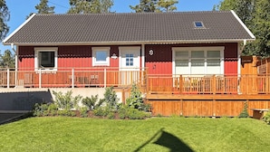 A two-story house with a red exterior, a grey roof, and a wooden deck. - Holiday Home in Lidköping (Lidköping)