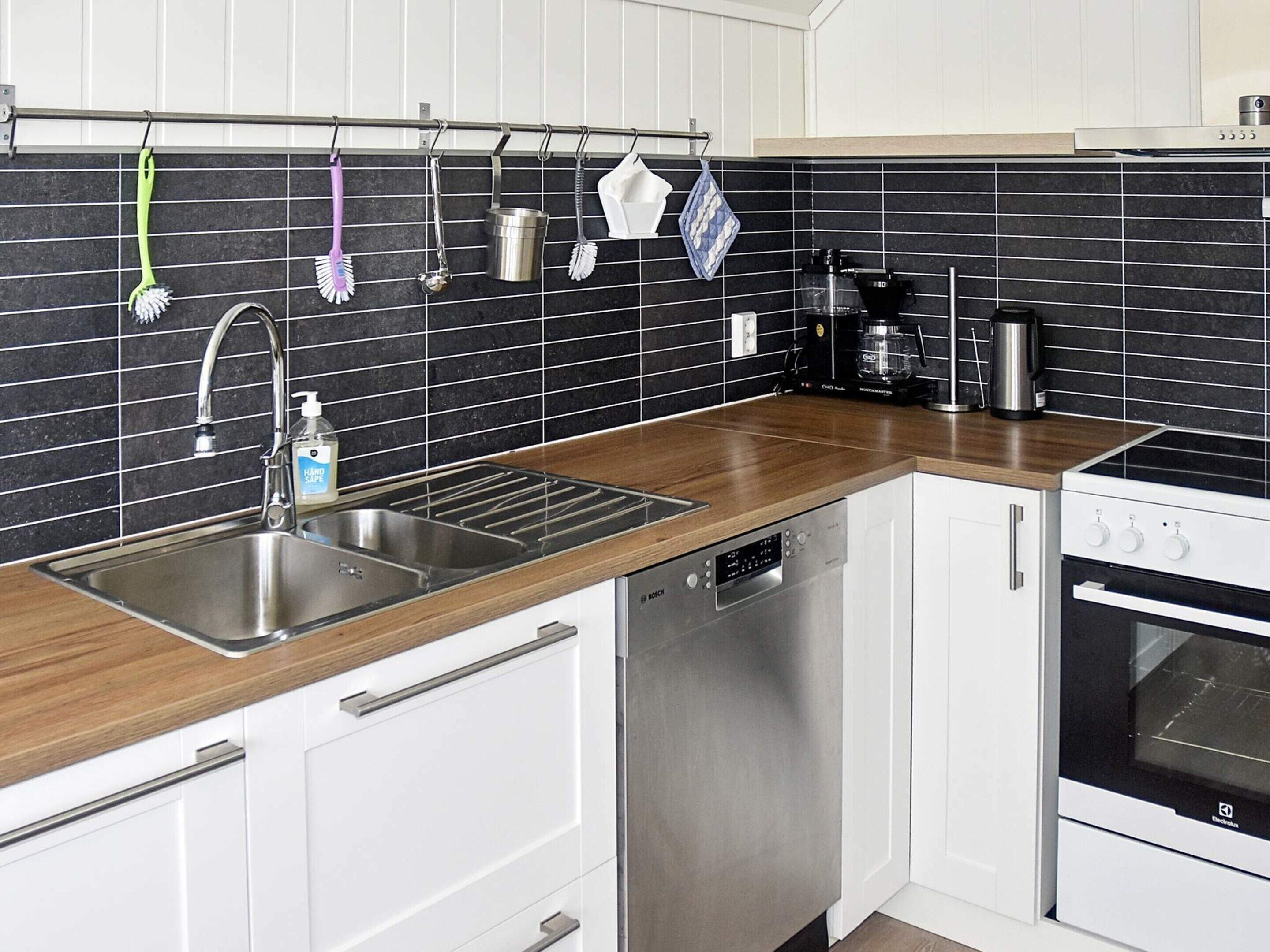 Una cocina moderna con un lavamanos de acero inoxidable, lavavajillas Bosch y un salpicadero de azulejos blanco y negro.