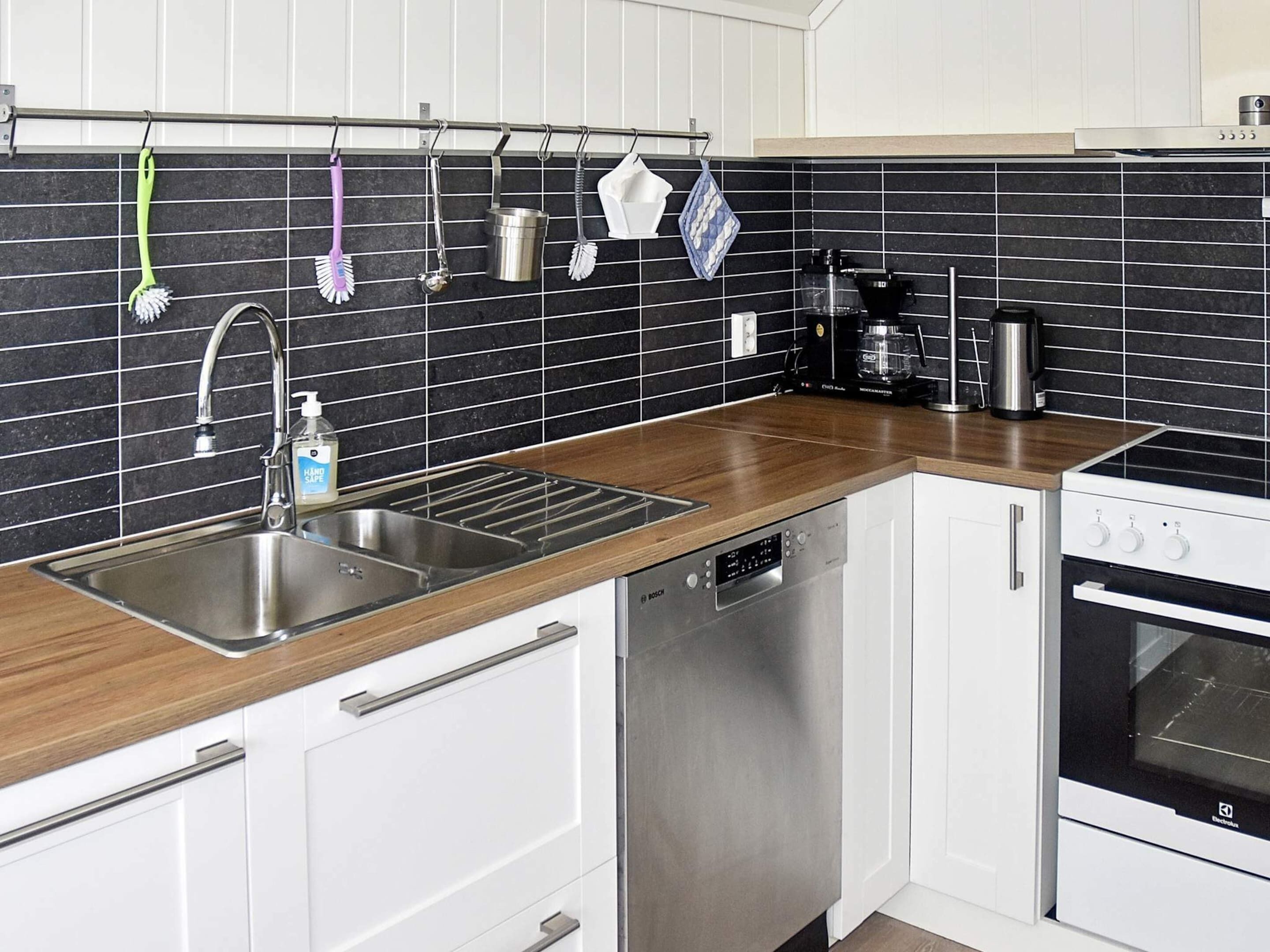 A modern kitchen with a stainless steel sink, Bosch dishwasher, and a black and white tiled backsplash.