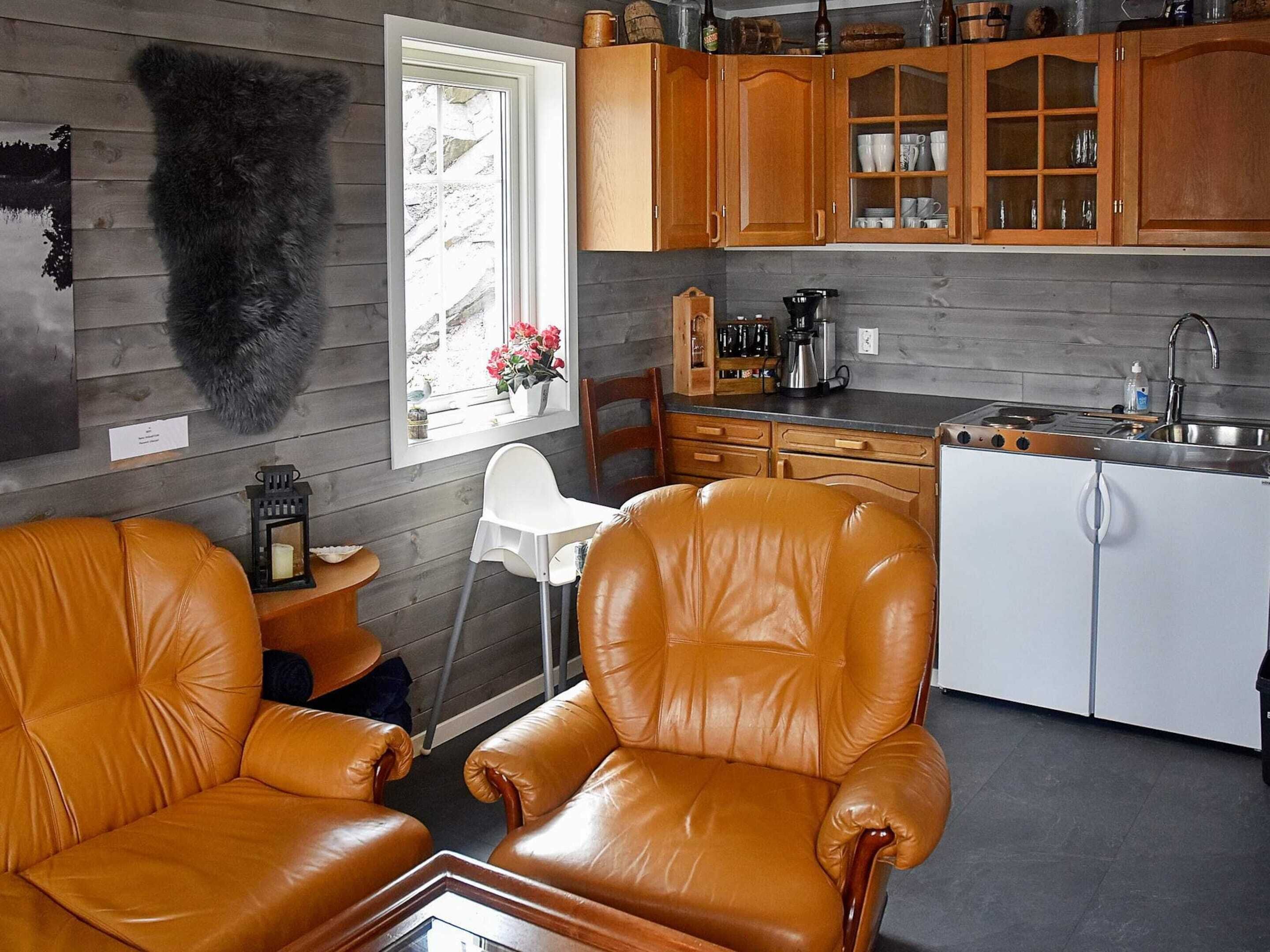 A modern kitchen with wooden cabinets, a white countertop, and a built-in stove. There is a leather chair and a small table with a candle.