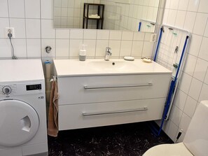 Un bagno moderno con un lavandino bianco, uno specchio, un porta asciugamani e una lavatrice.