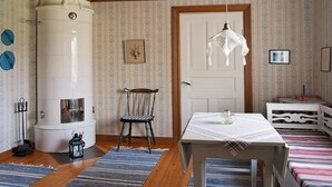 Quarto com fogão branco, cadeira de madeira, mesa com toalha de renda e tapetes listrados.
