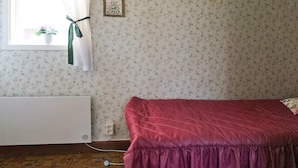 Quarto com cama, radiador, janela com cortinas e parede com padrão floral.