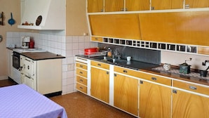 Cozinha compacta com armários de madeira, painel de azulejos e pequena área de refeições com mesa e cadeiras.