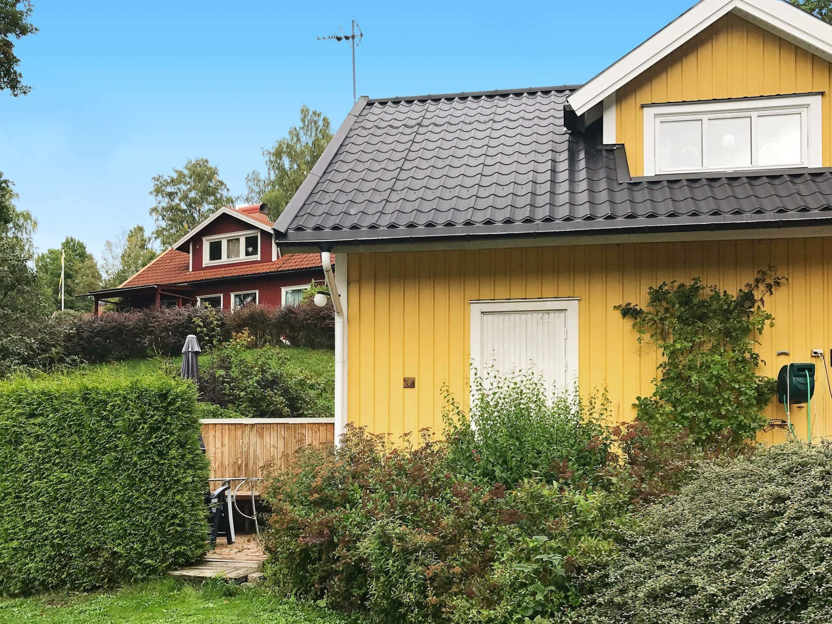 Ett gult hus med ett mörkt tak, omgivet av grönska och ett trästaket.