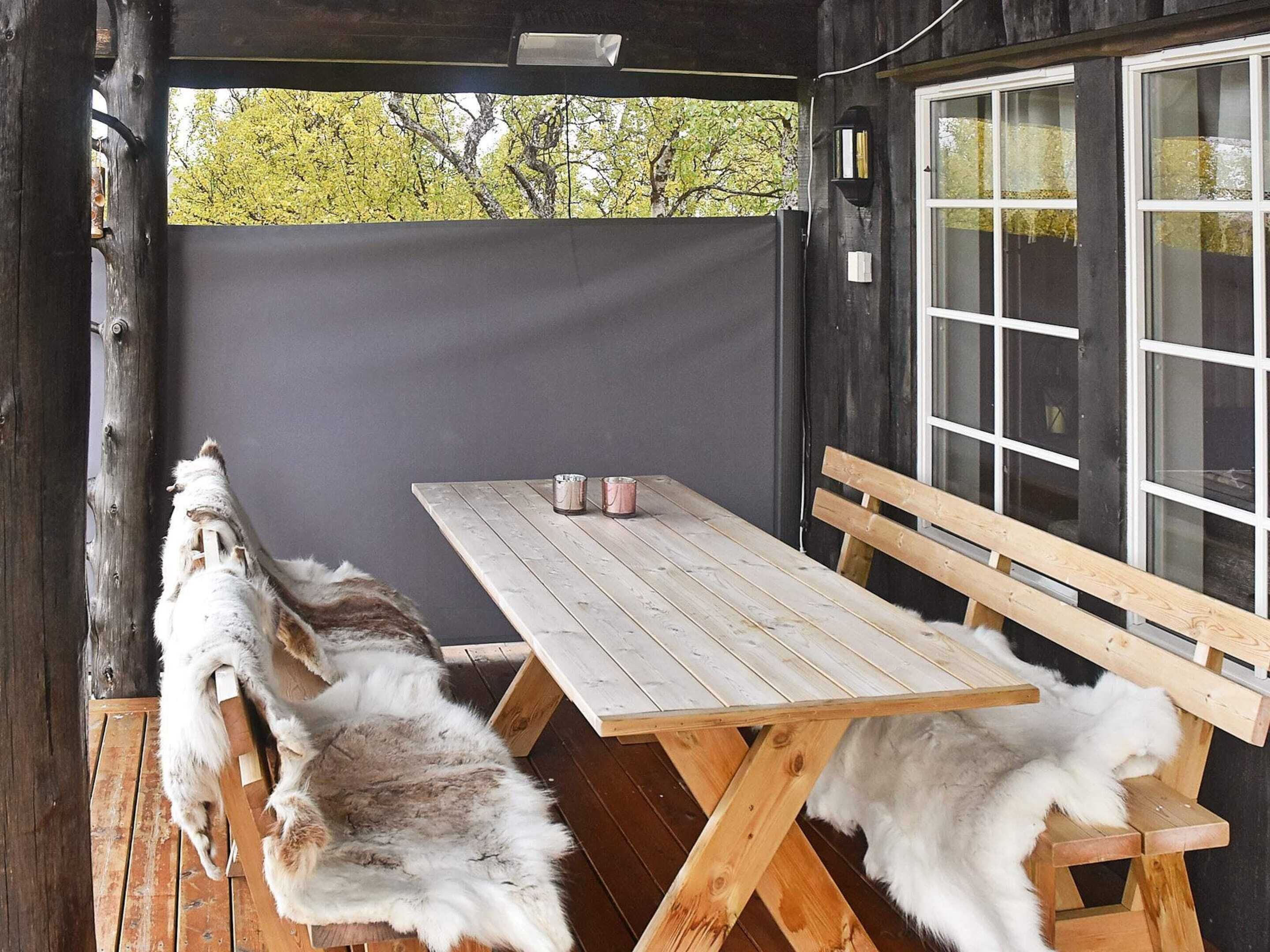 Una mesa de madera con bancos, un banco adicional y un ventanal con vistas a árboles.
