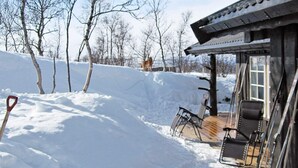 A cabin with a wooden deck and chairs, surrounded by snow-covered ground and leafless trees. - 4 Star Holiday Home in Rennebu (Rennebu)