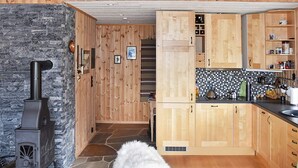 A cozy kitchen with wooden cabinets, a stone wall, and a black stove. - 4 Star Holiday Home in Rennebu (Rennebu)